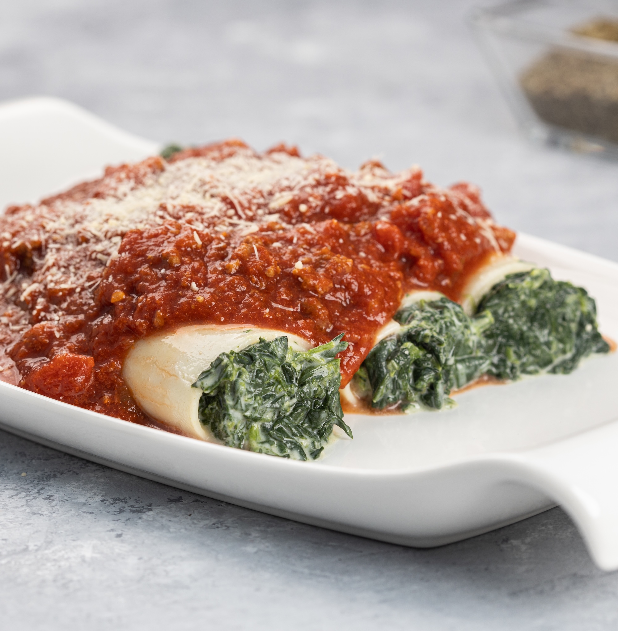 A closeup shot of a Cannelloni dish stuffed with spinach and ricotta served with bolognese sauce