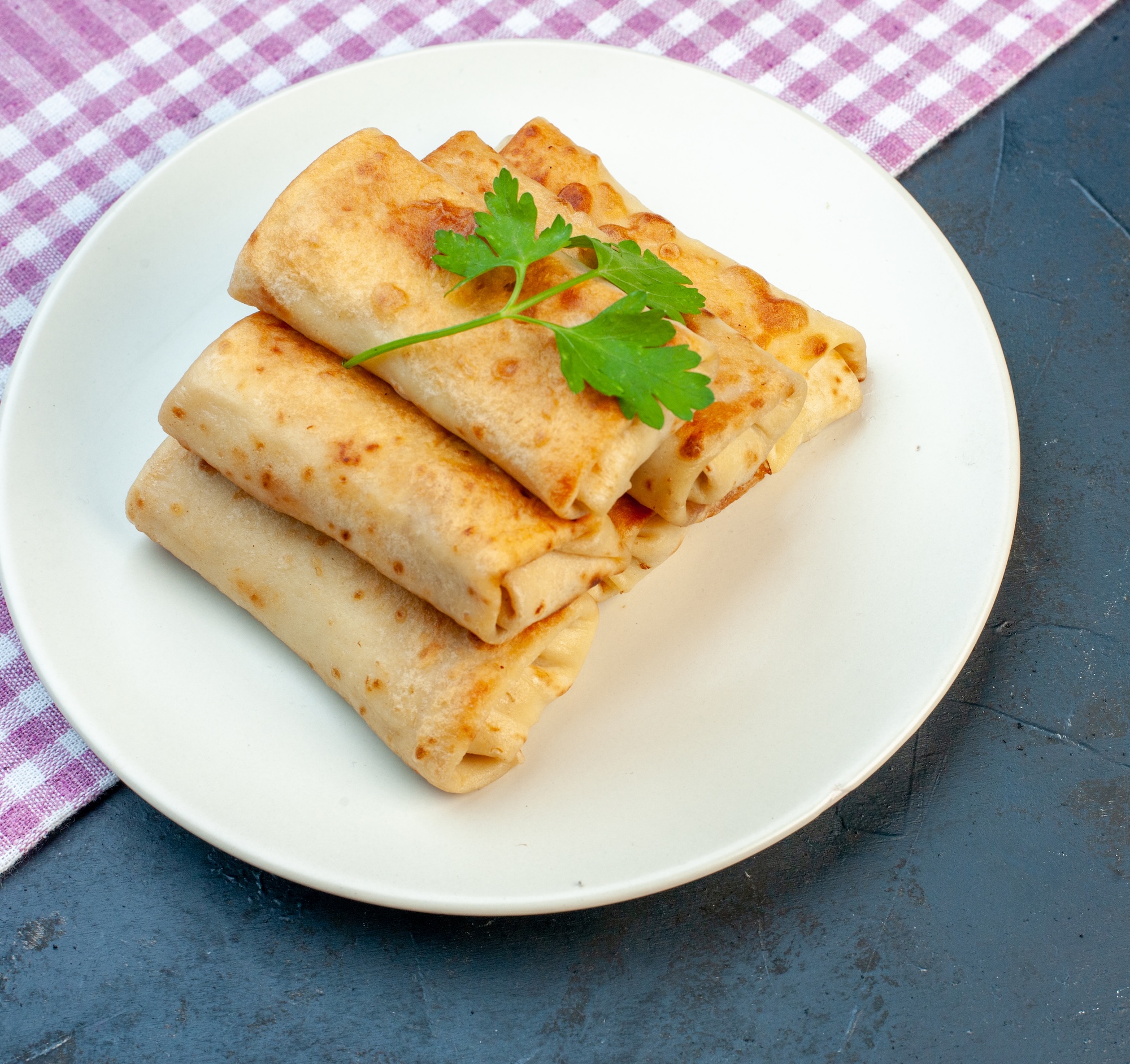 Side view of lavash wraps on a plate with green on purple stripped towel on the right side on black background